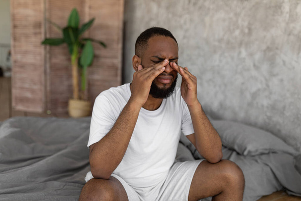 Black man suffering from headache or migraine in bed - 写真・画像