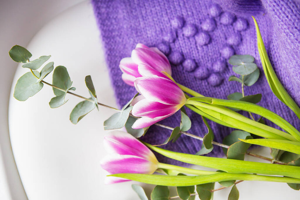 Hermoso ramo de primavera de tulipanes morados con eucalipto en una silla blanca junto con un suéter morado. Humor de primavera, 8 de marzo. Postal para las vacaciones - Foto, Imagen