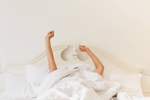 Mujer en la cama debajo de la manta estirando la mano después de despertar. - Foto, imagen