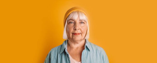 Beautiful 50s woman with blonde hair in stylish casual clothes with copyspace looking at the camera on yellow color background studio portrait. - 写真・画像