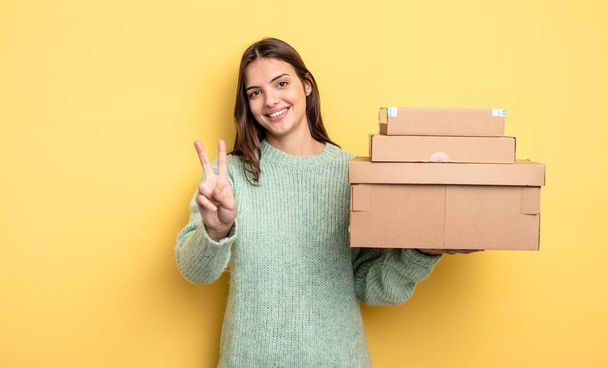 pretty woman smiling and looking friendly, showing number two packages boxes concept - Foto, Bild