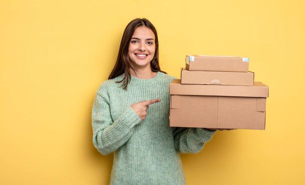 pretty woman smiling cheerfully, feeling happy and pointing to the side packages boxes concept - Foto, Bild
