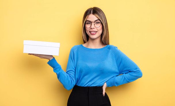 pretty woman smiling happily with a hand on hip and confident. holding white box - Foto, Imagen