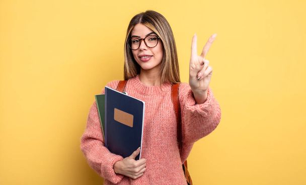pretty student woman smiling and looking friendly, showing number two. books and backpack - 写真・画像