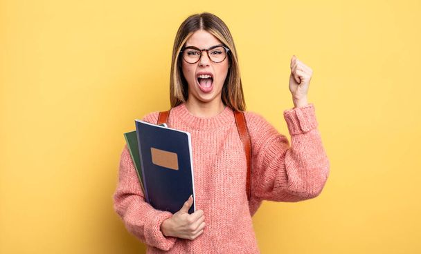 pretty student woman shouting aggressively with an angry expression. books and backpack - Fotoğraf, Görsel