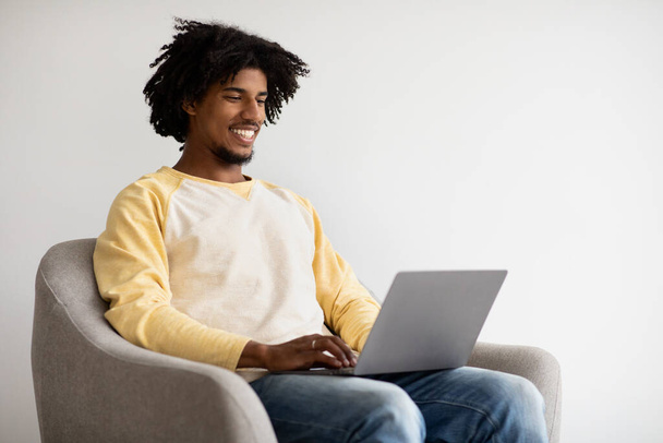 Carrière freelance. Noir Millennial Guy travailler avec ordinateur portable tout en étant assis dans la chaise - Photo, image