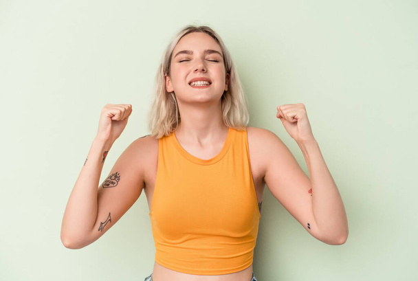 Young caucasian woman isolated on green background celebrating a victory, passion and enthusiasm, happy expression. - Photo, Image