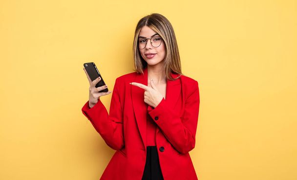 businesswoman smiling cheerfully, feeling happy and pointing to the side. smartphone concept - Foto, afbeelding
