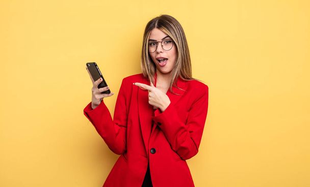 businesswoman looking excited and surprised pointing to the side. smartphone concept - Foto, afbeelding