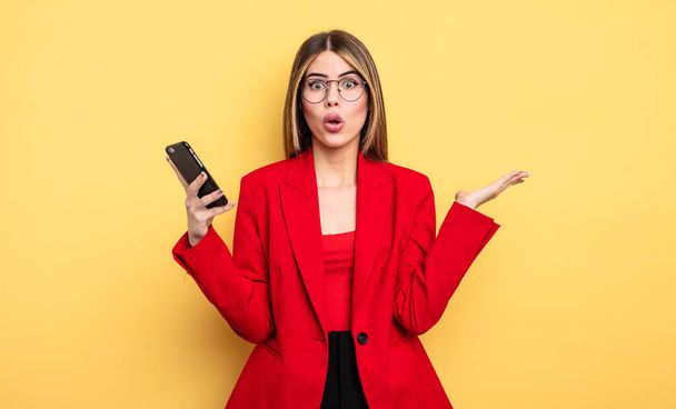 businesswoman looking surprised and shocked, with jaw dropped holding an object. smartphone concept - Foto, imagen