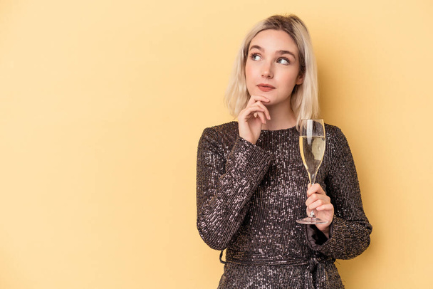 Young caucasian woman celebrating new year isolated on yellow background looking sideways with doubtful and skeptical expression. - Photo, Image