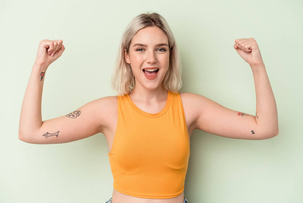 Young caucasian woman isolated on green background showing strength gesture with arms, symbol of feminine power - Foto, afbeelding