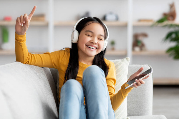 Joyful chinese child listening to music on cellpohne - Foto, imagen