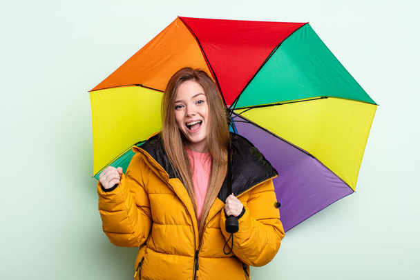 redhair woman feeling shocked,laughing and celebrating success. umbrella concept - Foto, afbeelding