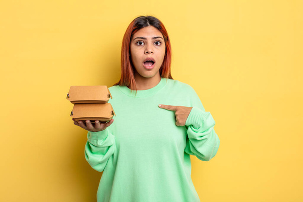 hispanic woman looking shocked and surprised with mouth wide open, pointing to self. take away burgers concept - Photo, image