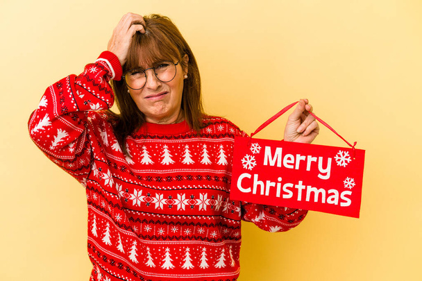 Middle age caucasian woman holding merry Christmas placard isolated on yellow background being shocked, she has remembered important meeting.  - Valokuva, kuva