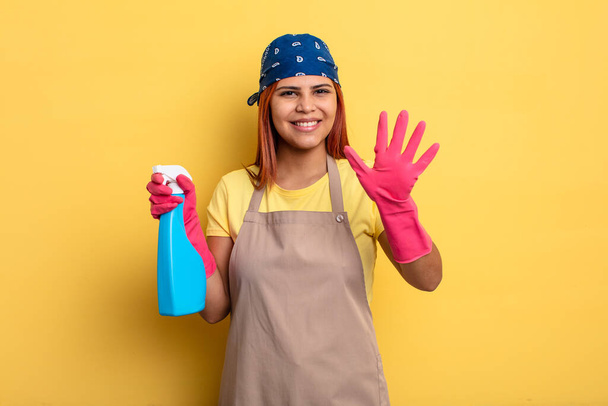 hispanic woman smiling and looking friendly, showing number five. cleaning and housekeeper concept - Foto, imagen