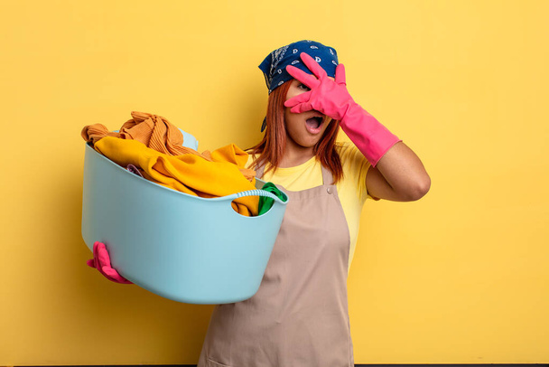 housekeeper looking shocked, scared or terrified, covering face with hand. washing clothes concept - Foto, Imagem