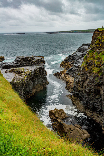 Water inlet on a rocky cliff on the coastal walk route from Doolin to the Cliffs of Moher, rainy day with a gray sky with heavy clouds in County Clare, Ireland. Geosites and Geopark, Wild Atlantic Way - Foto, afbeelding