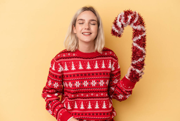 Mladá běloška žena drží velké vánoční hůl izolované na žlutém pozadí se směje a baví. - Fotografie, Obrázek