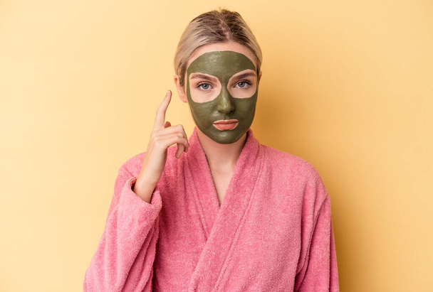 Young caucasian woman wearing face mask isolated on yellow background pointing temple with finger, thinking, focused on a task. - Foto, immagini