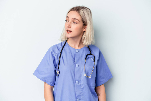 Young nurse woman isolated on blue background looks aside smiling, cheerful and pleasant. - Photo, Image