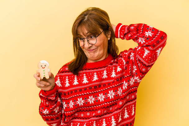 Middle age caucasian woman holding a Christmas cookies isolated on yellow background - Foto, afbeelding