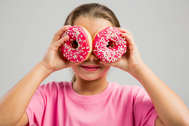 Studio portrait of a beautiful little girl looking through a donut - Photo, image