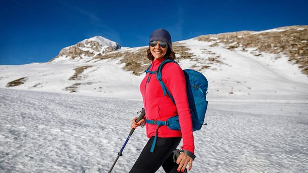 Halve lengte portret van een lachende vrouw als ze alleen door de sneeuw in de bergen loopt, op een zonnige winterdag. Sportman in de sneeuw. Horizontale banner - Foto, afbeelding