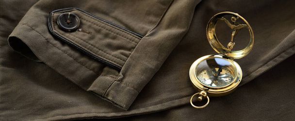 Zabytkowy złoty kompas (zegar słoneczny) i stary brązowy płaszcz z bliska. Vintage martwa natura. Żeglarstwo, akcesoria turystyczne, sztuka koncepcyjna, kolekcja, ubrania, sprzęt, zasoby graficzne - Zdjęcie, obraz