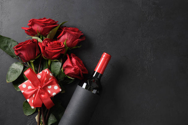 Valentine's day gift, red wine, bouquet of roses on black background. Greeting card with copy space. View from above. - Foto, Imagen