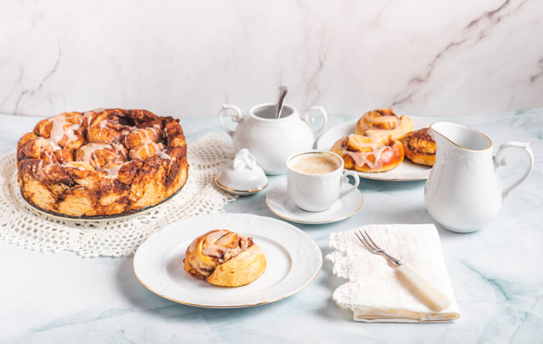 Rouleaux de cannelle faits maison sur une assiette blanche sur une table blanche avec du café et des pains à pâtisserie pour le petit déjeuner. Recette traditionnelle suédoise et danoise. - Photo, image