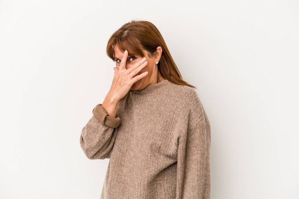 Middle age caucasian woman isolated on white background blink at the camera through fingers, embarrassed covering face. - Photo, Image