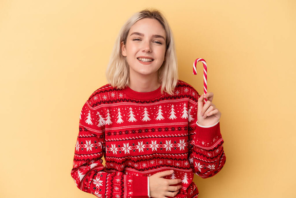 Young caucasian woman holding a christmas stick isolated on yellow background laughing and having fun. - Photo, Image