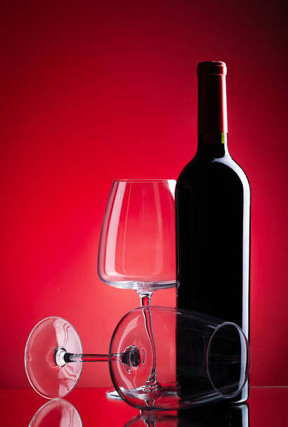 Rode wijn glazen en fles over rode achtergrond - Foto, afbeelding