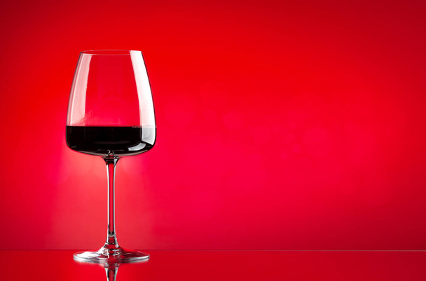 Rood wijnglas over rode achtergrond met kopieerruimte - Foto, afbeelding