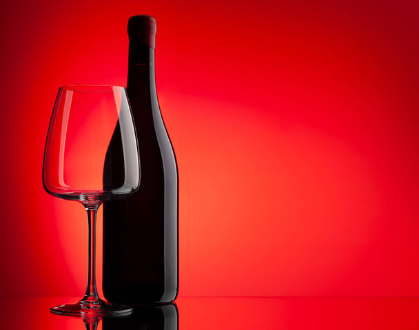 Červené víno sklo a láhev přes červené pozadí s kopírovacím prostorem - Fotografie, Obrázek