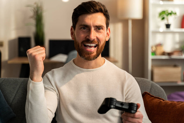 That is my best round. Excited young handsome man playing video game and keeping mouth open while sitting on the couch at home  - Fotografie, Obrázek