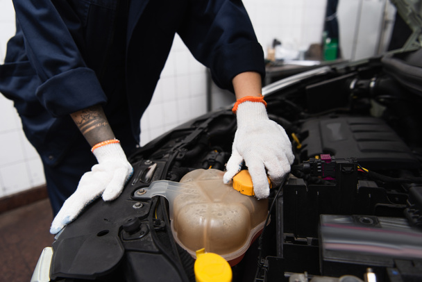 Cropped view of mechanic in gloves unscrewing cap in car in service  - 写真・画像