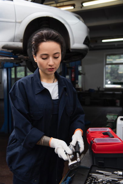 Workwoman in gloves taking tool near toolbox in car service  - Photo, Image