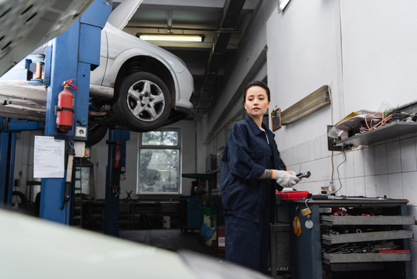 Mechanic holding tool and looking at blurred car in service  - 写真・画像