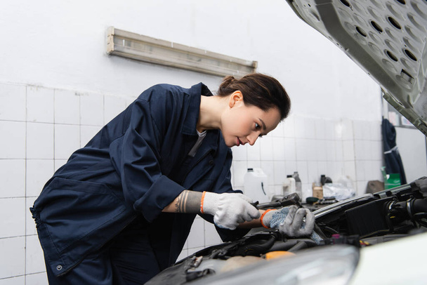 Tattooed mechanic using wrench while working with auto in service  - Zdjęcie, obraz