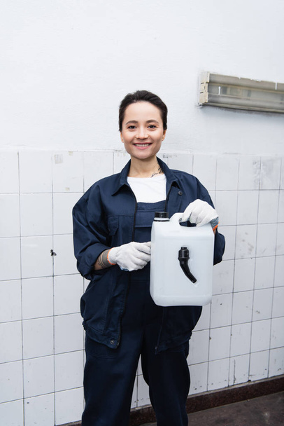 Usmívající se mechanik v uniformě drží kanystr v autoservisu  - Fotografie, Obrázek