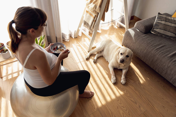Pregnant woman working at home resting and eating healthy food in the company of her best friend - Φωτογραφία, εικόνα
