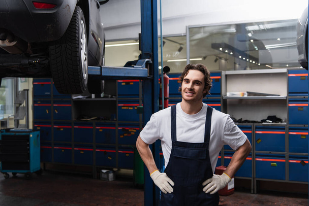 Smiling mechanic holding hands on hips in garage  - 写真・画像