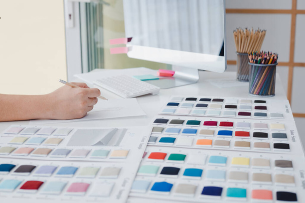 Hand of the clothing designer is drawing the clothing layout to be tailored to the customer as accepted by the client on table of clothing designers with computer, shades of start up business concept. - Foto, imagen