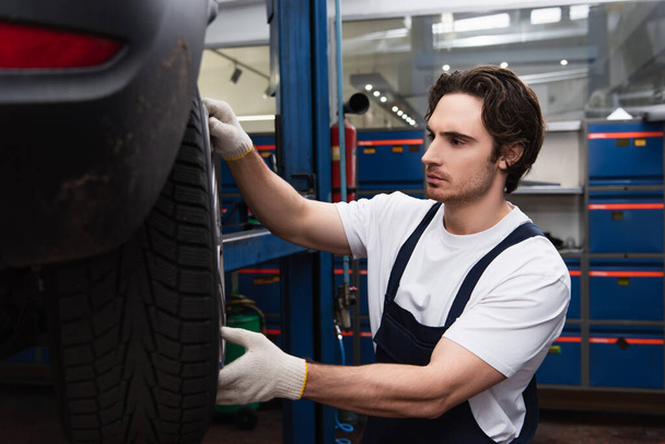 Young mechanic working with wheel disk and car in garage  - Photo, image
