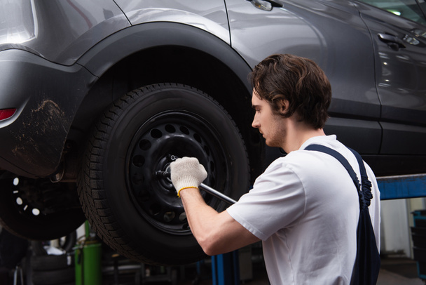 Side view of workman unscrewing car wheel in garage  - Fotografie, Obrázek