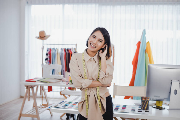 Kollarını kavuşturup ofiste başarılı bir şekilde gülümseyen mutlu Asyalı tasarımcı kadın. Başlangıç tasarımcısı konsepti. Kıyafet tasarımcıları stüdyoda çalışıyor.. - Fotoğraf, Görsel
