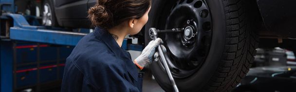 Workwoman in glove working with car wheel and wrench in garage, banner  - 写真・画像